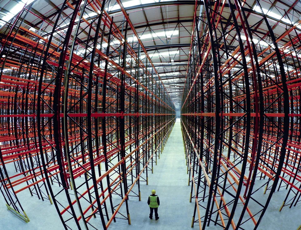 Worker standing in a large empty warehouse with tall industrial racking.