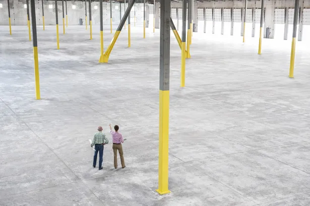 Two people inspecting the interior of a large empty warehouse.