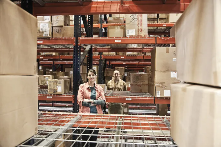 Two warehouse workers standing among racks of boxed inventory.