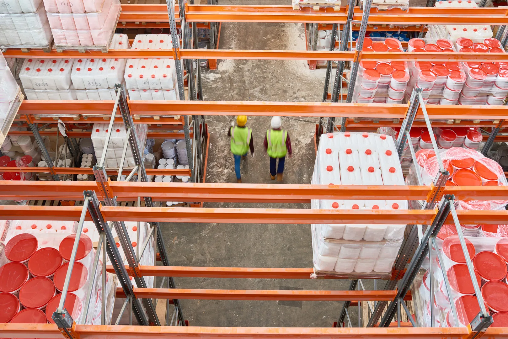 Warehouse storage racks with industrial containers and workers in safety gear.